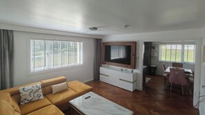 En stue med sofa, fjernsyn, sofabord og et spiseområde med stole.