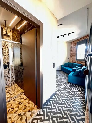 A modern interior with a geometric patterned floor, a blue sofa, and a shower area with a geometric wall design. - #ALS_ON AIR LUXURY ROOFTOP (Thessaloniki)