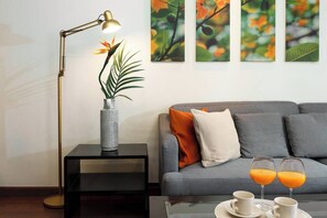 Ein modernes Wohnzimmer mit einer Couch, einem Beistelltisch mit einer Lampe, einer Vase mit einer Pflanze und einem Couchtisch mit zwei Gläsern Orangensaft und zwei Tassen.