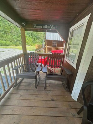 A wooden cabin with a porch, a sign reading 'Welcome to Our Cabin,' and a red car parked outside.