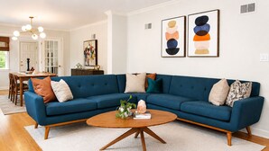 A living room with a blue sectional sofa, a wooden coffee table, and two abstract paintings on the wall. - Welcome to Brookside Mod Cottage: Spacious and group friendly! (Kansas City)