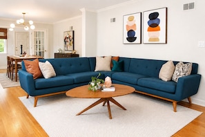 A living room with a blue sectional sofa, a wooden coffee table, and two abstract paintings on the wall. - Welcome to Brookside Mod Cottage: Spacious and group friendly! (Kansas City)