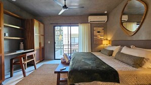 Ein Hotelzimmer mit Bett, Schreibtisch, Stuhl, Deckenventilator, Klimaanlage, Spiegel und Blick durch eine Schiebetür.