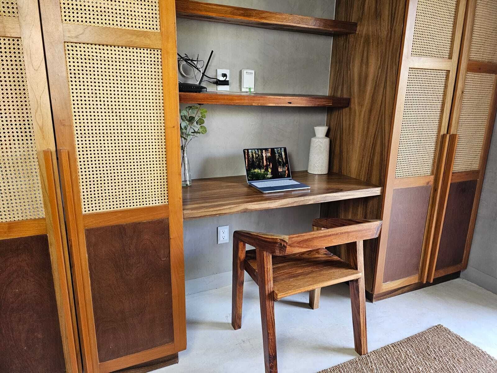 Una habitación con un escritorio de madera, una computadora portátil, un florero y una planta.
