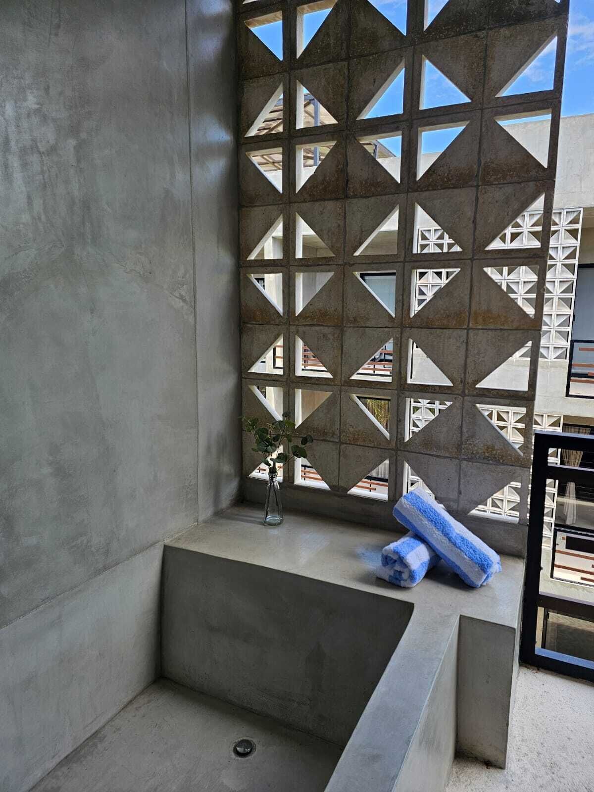 Une salle de bain moderne avec une grande baignoire, un mur orné d’un motif géométrique et une petite fenêtre agrémentée d’une plante.