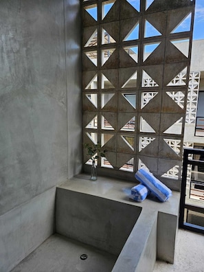 Ein modernes Badezimmer mit einer großen Badewanne, einer Wand mit geometrischem Muster und einem kleinen Fenster mit Pflanze.