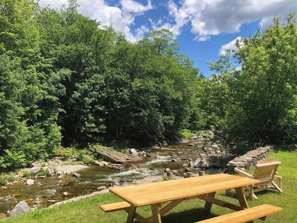 Una mesa de picnic y sillas junto a un río en una zona boscosa.