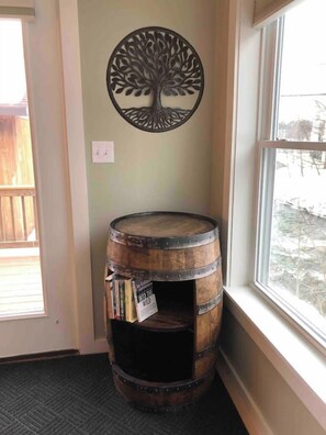 A corner room with a wooden barrel bookshelf, a wall-mounted tree decoration, and a window with a view of the outdoors.