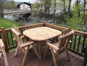 A wooden deck with a table and chairs overlooking a river and buildings. - Trout River Lodge - Discount Jay Peak Lift Tix (Montgomery)