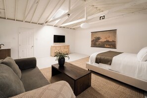 A modern room with a bed, sofa, wooden dresser, television, and artwork on the wall. - The Manchester Retreat (Los Angeles)