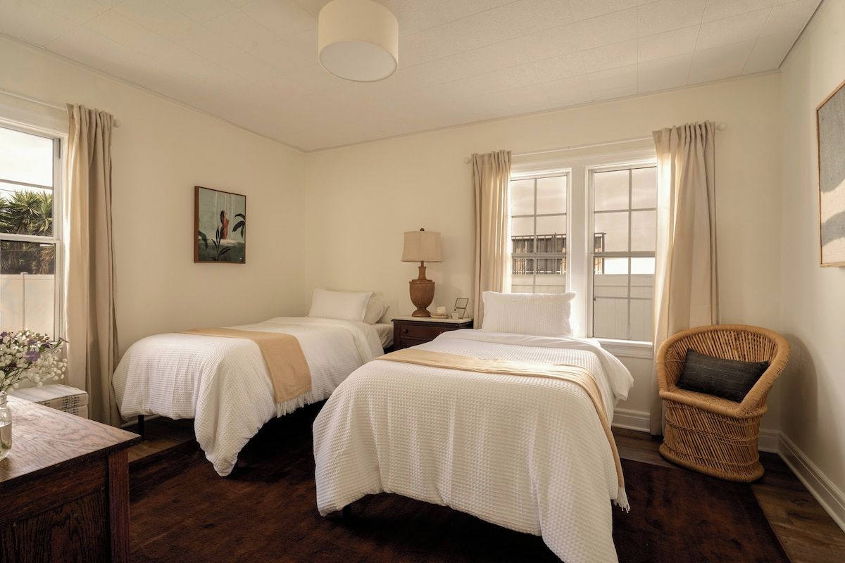 A hotel room with two beds, a chair, a desk, and a window with curtains.