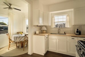 A kitchen with white cabinets, a stove, a window, and a dining area with chairs and a table.