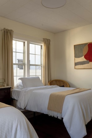 A hotel room with two beds, a window with curtains, a bedside table, and a wall-mounted painting. - The Manchester Retreat (Los Angeles)