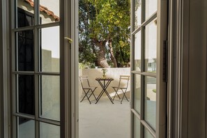 Puerta abierta que da a un patio con una mesa, sillas, un árbol y una pared blanca.