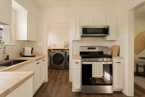 A kitchen with white cabinets, a microwave, a stove, and a washing machine. - The Manchester Retreat (Los Angeles)