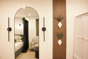 A hallway with a mirror, a bed, a sofa, a plant, and a door. - Cozy 1-Bedroom Apartment Near NYC & MetLife + WiFi + Laundry (Jersey City)