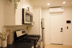 A kitchen with white cabinets, a stove, a microwave, and a refrigerator. - Cozy 1-Bedroom Apartment Near NYC & MetLife + WiFi + Laundry (Jersey City)