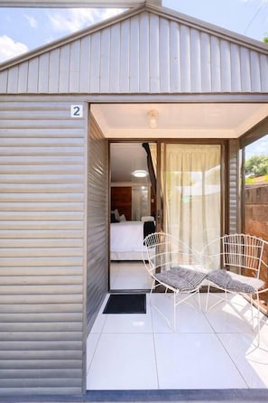A modern building with a number '2' sign, a sliding door entrance, a bed, and two white chairs outside.