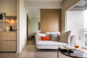 A modern living room with a sofa, a coffee table, and a view through a large window. - Sea View Balcony Condo | Gym + King Bed | 1min to Private Beach (Sattahip)
