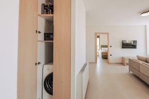 A modern apartment with a laundry area, a living room with a sofa, and a hallway leading to a bathroom.