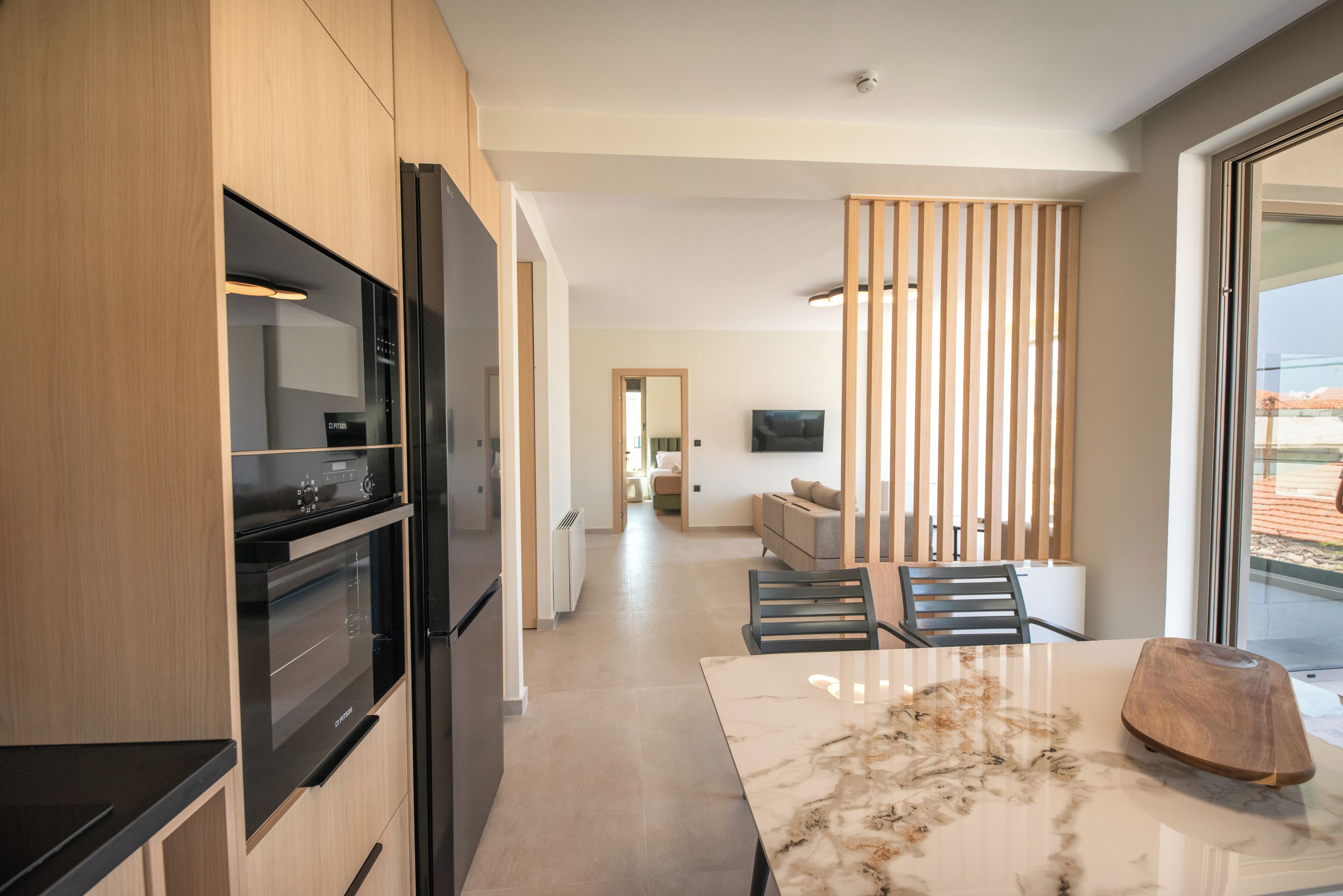 Een moderne keuken met inbouwapparatuur, een eetgedeelte met een marmeren tafel en uitzicht door een raam.