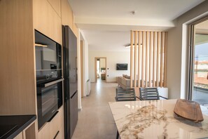 Una cocina moderna con electrodomésticos integrados, un comedor con mesa de mármol y vistas a través de una ventana.