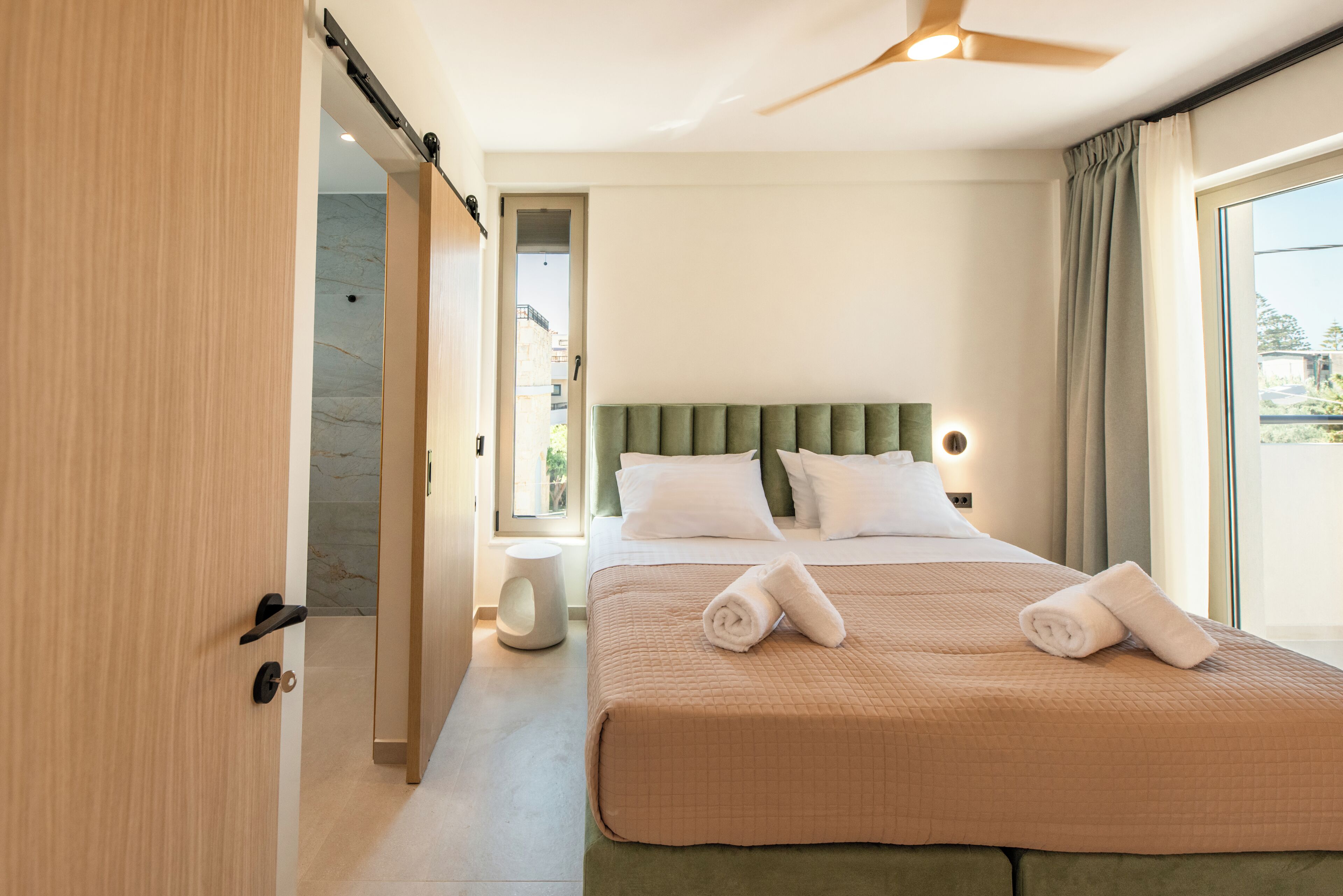 Una habitación de hotel con cama, mesita de noche, lámpara de pared y vistas al exterior.