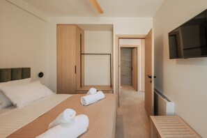 Habitación de hotel con dos camas, un televisor, un armario de madera y un baño visible a través de una puerta abierta.