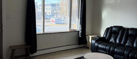 Un salon moderne avec un canapé en cuir noir, une table basse ronde et une grande fenêtre avec des rideaux.