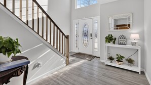A staircase leading to a door with a decorative glass panel, a console table with plants and a lamp, and a mirror above it. - Spacious 4-bedroom house in charming Arrowhead Lake w/ Fire Pit, Gameroom, Pool (pocono lake)