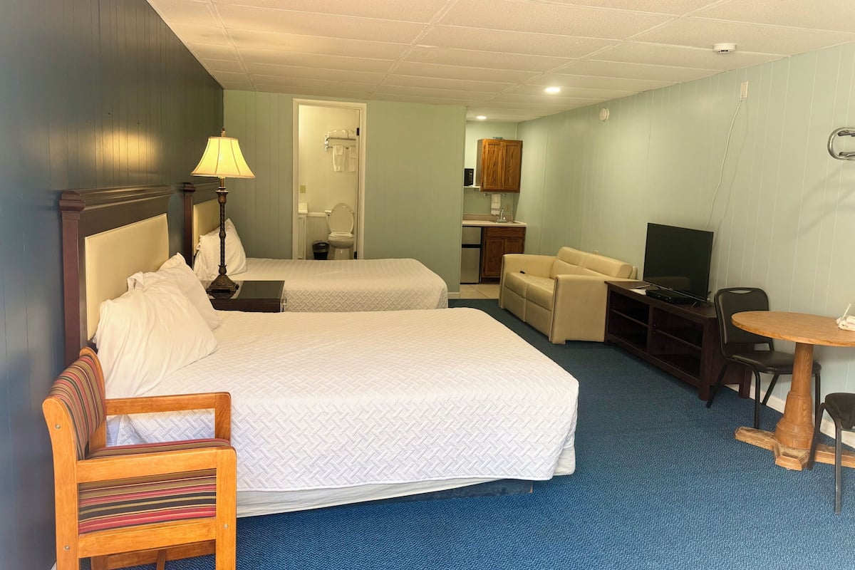 A hotel room with two beds, a sofa, a TV, a small table, and a kitchenette.