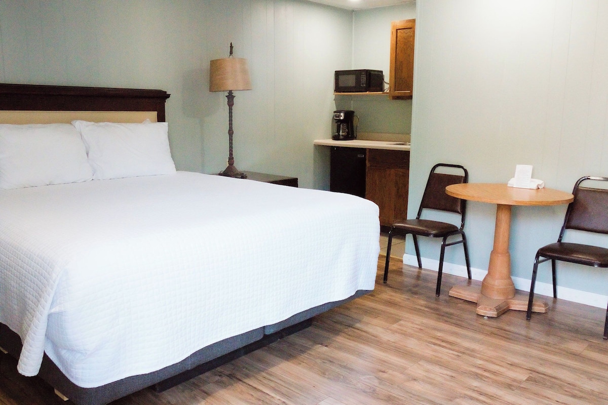 A hotel room with a bed, a desk, a microwave, a coffee maker, and two chairs.