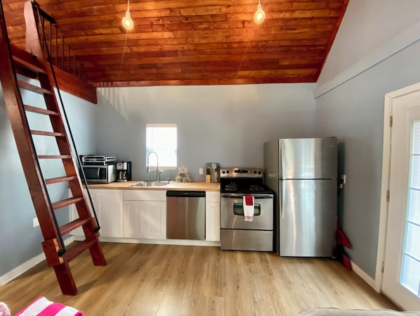 A kitchen with wooden ceiling, stainless steel appliances, a dishwasher, and a wooden ladder. - Gregory's Lodging and General Store (Shelbyville)