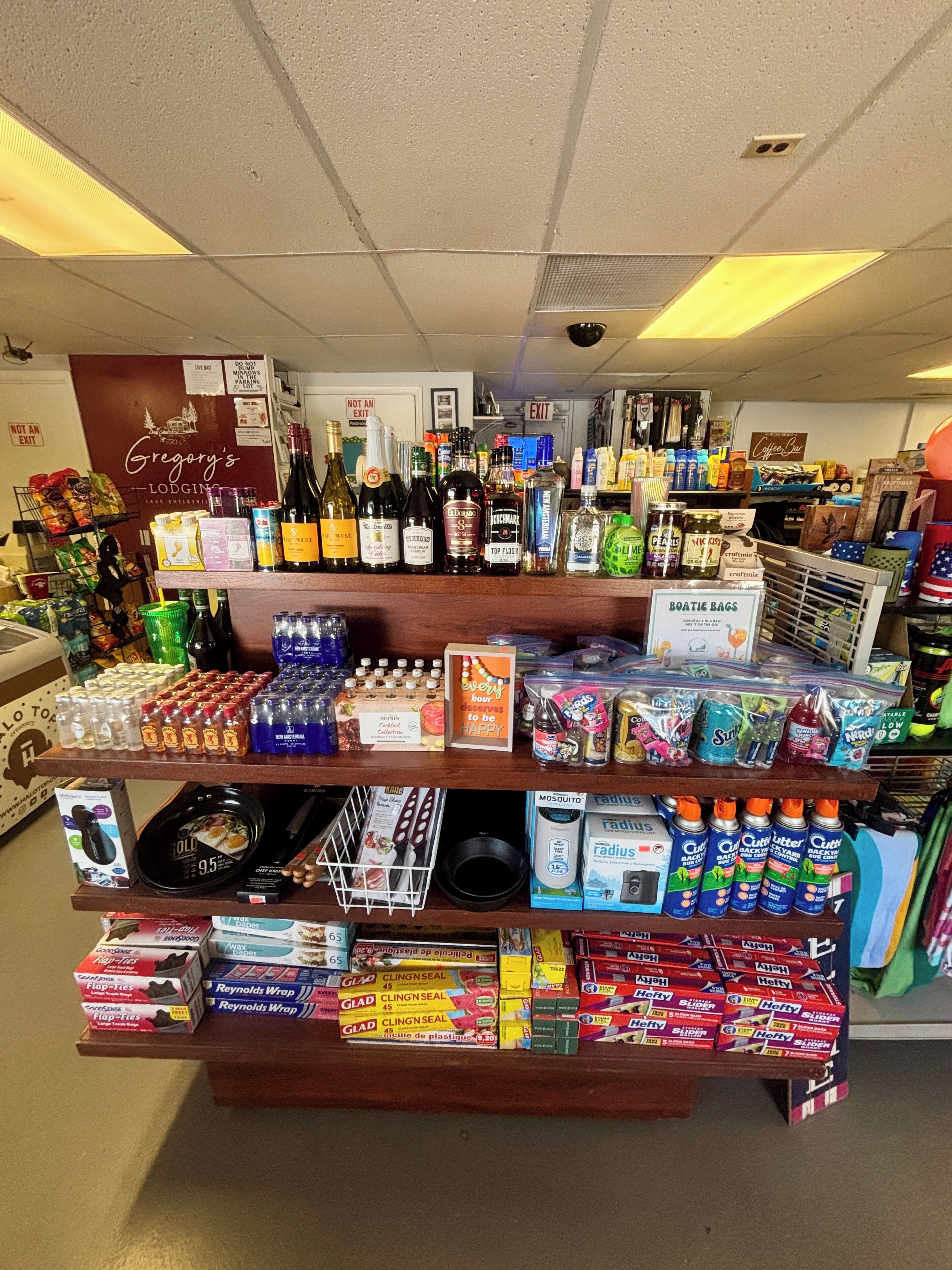A liquor store with shelves stocked with various bottles and cans, a 'BOATIE BAGS' sign, and a 'Gregory's Lodging' sign in the background.