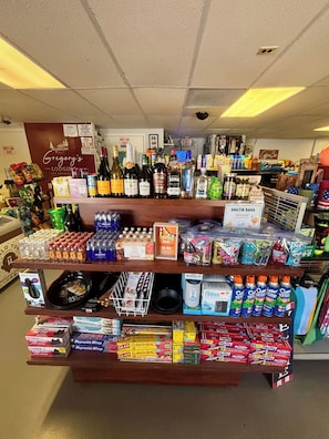 A liquor store with shelves stocked with various bottles and cans, a 'BOATIE BAGS' sign, and a 'Gregory's Lodging' sign in the background. - Gregory's Lodging and General Store (Shelbyville)