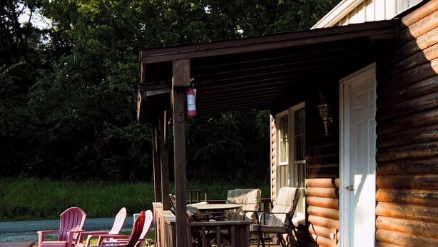 A wooden cabin with a covered patio, outdoor seating, and a garden with flowers. - Gregory's Lodging and General Store (Shelbyville)