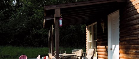 Eine Holzhütte mit überdachter Veranda, Gartenmöbeln im Freien und einem Blumengarten.