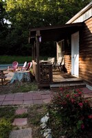 Una cabaña de madera con un porche cubierto, mobiliario exterior y un jardín lleno de flores.