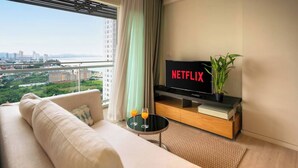 Ein modernes Wohnzimmer mit einer Couch, einem Fernseher mit 'NETFLIX', einem kleinen Tisch mit Gläsern und einer Pflanze.