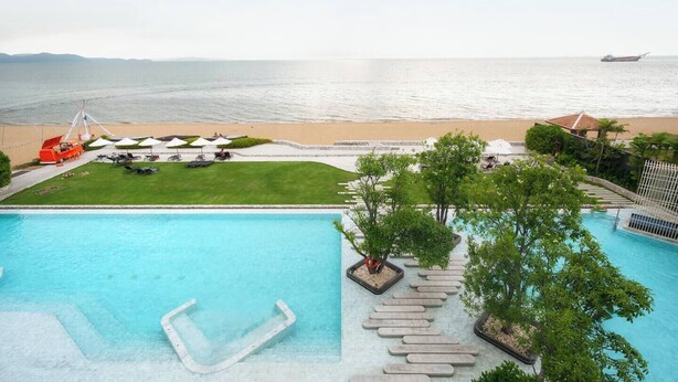 Ein Pool mit freiem Blick auf das Meer, ein Strandbereich mit Sonnenschirmen und ein Rettungsturm.