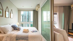Ein Hotelzimmer mit Bett, Sessel, Fernseher und Balkon mit Blick auf die Stadt.