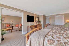 Quarto de hotel com cama, escrivaninha, cadeira, sofá e televisão.