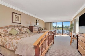 Quarto de hotel com cama, escrivaninha, poltrona, televisão e varanda com vista.