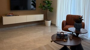 Ein modernes Wohnzimmer mit Flachbildfernseher, Topfpflanze, Sofa, Couchtisch und dekorativer Vase.