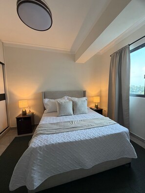 Ein Hotelzimmer mit Bett, zwei Nachttischen, einem Fenster mit Vorhängen und einer Deckenleuchte.