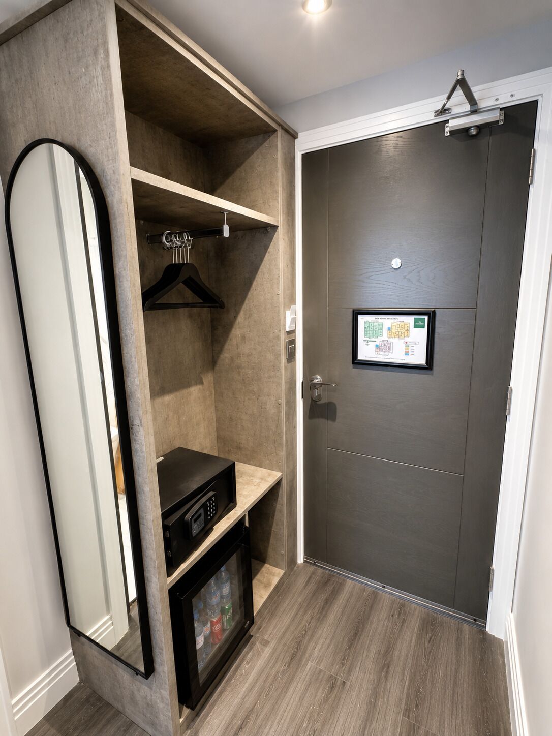 A hotel room with a wardrobe, a coat rack, a mirror, and a small shelf with bottled water.
