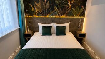A hotel room with a large bed, a nightstand with a lamp, a wall-mounted air conditioner, and a window with curtains.