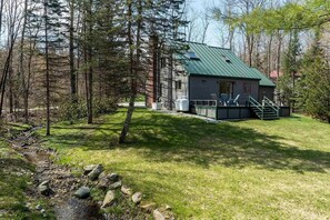 A cabin with a metal roof, surrounded by trees, a small porch, and a stone wall.