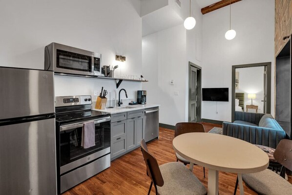 Una cucina moderna con elettrodomestici in acciaio inossidabile, una zona pranzo con tavolo rotondo e un soggiorno con divano e televisore.