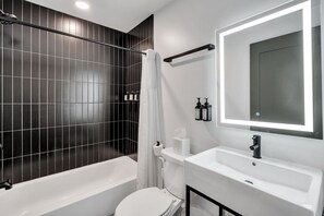 Un bagno moderno con vasca, water e uno specchio grande.